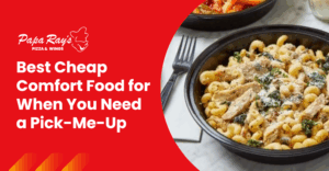 A bowl of cavatappi pasta topped with grilled chicken, spinach, mushrooms, and parmesan cheese, served as a warm and affordable comfort food option.