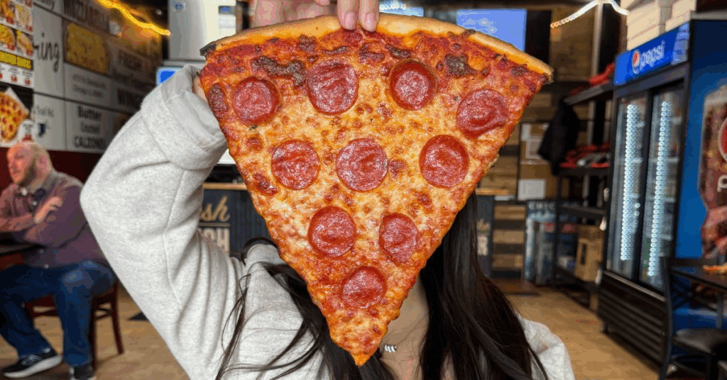  “Customer holding a Papa Ray’s Monster Slice with cheese pull”