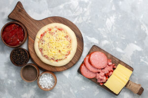 top view raw pizza with cheese different seasonings light white desk