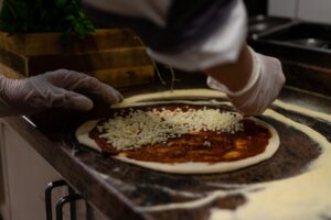 The Original Chicago Pizza in Cook County: What Makes It So Iconic? 2 Cheese being layered onto pizza dough before baking.