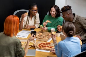 Group Ordering Restaurants: The Best Takeout Food for Large Groups 2 Office team eating pizza together at a shared table.