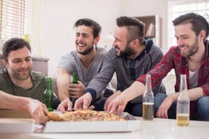 Win Tickets to Bears vs. Patriots: Papa Ray's October Giveaway 2 Four friends laughing together while eating pizza and drinking beer at home.